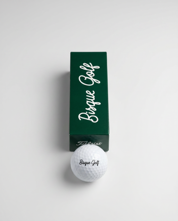 Titleist Pro V1 golf ball with Bisque Golf logo beside a green Bisque Golf sleeve